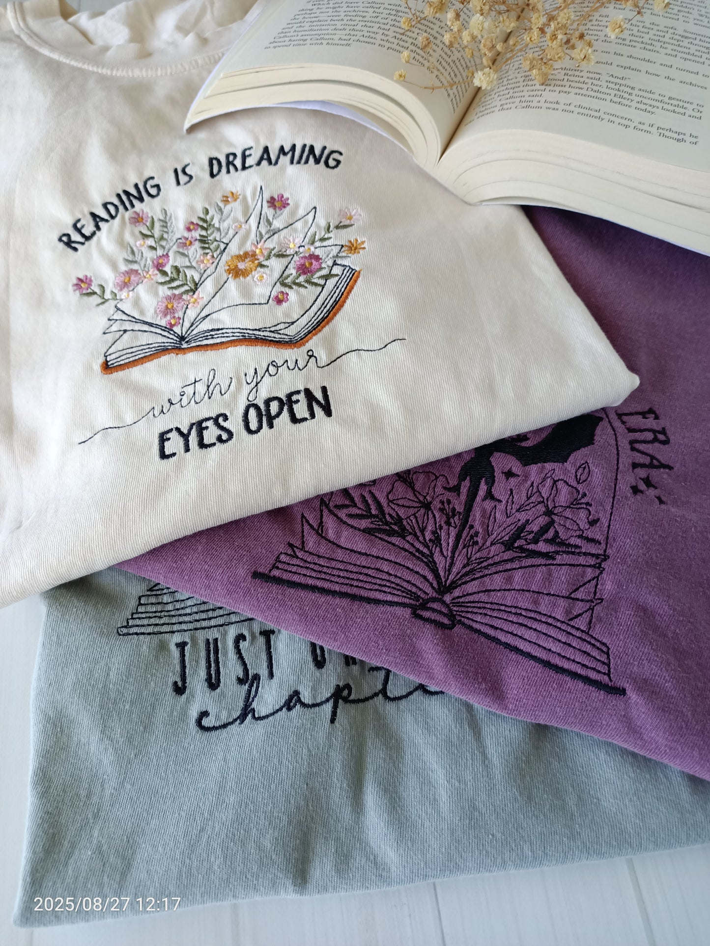 Stack of t-shirts with book-themed designs and text on a white surface.
